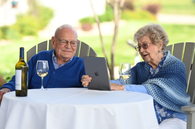 Couple in blue looking at an iPad, enjoying a glass of white wine