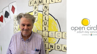 Rick, a longtime member of Open Circle Hopkins, stands smiling in front of a mural, representing his contributions and connection to the community.