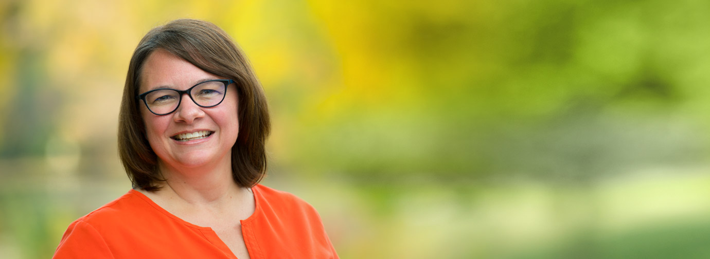 Smiling woman in glasses and an orange blouse outdoors.
