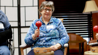 Senior woman smiling while playing a maraca in a drum circle.