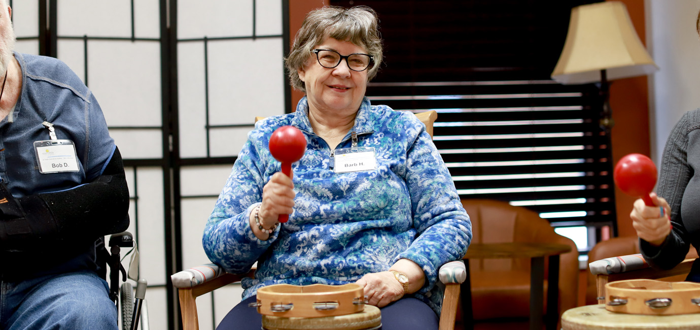 Senior woman smiling while playing a maraca in a drum circle.